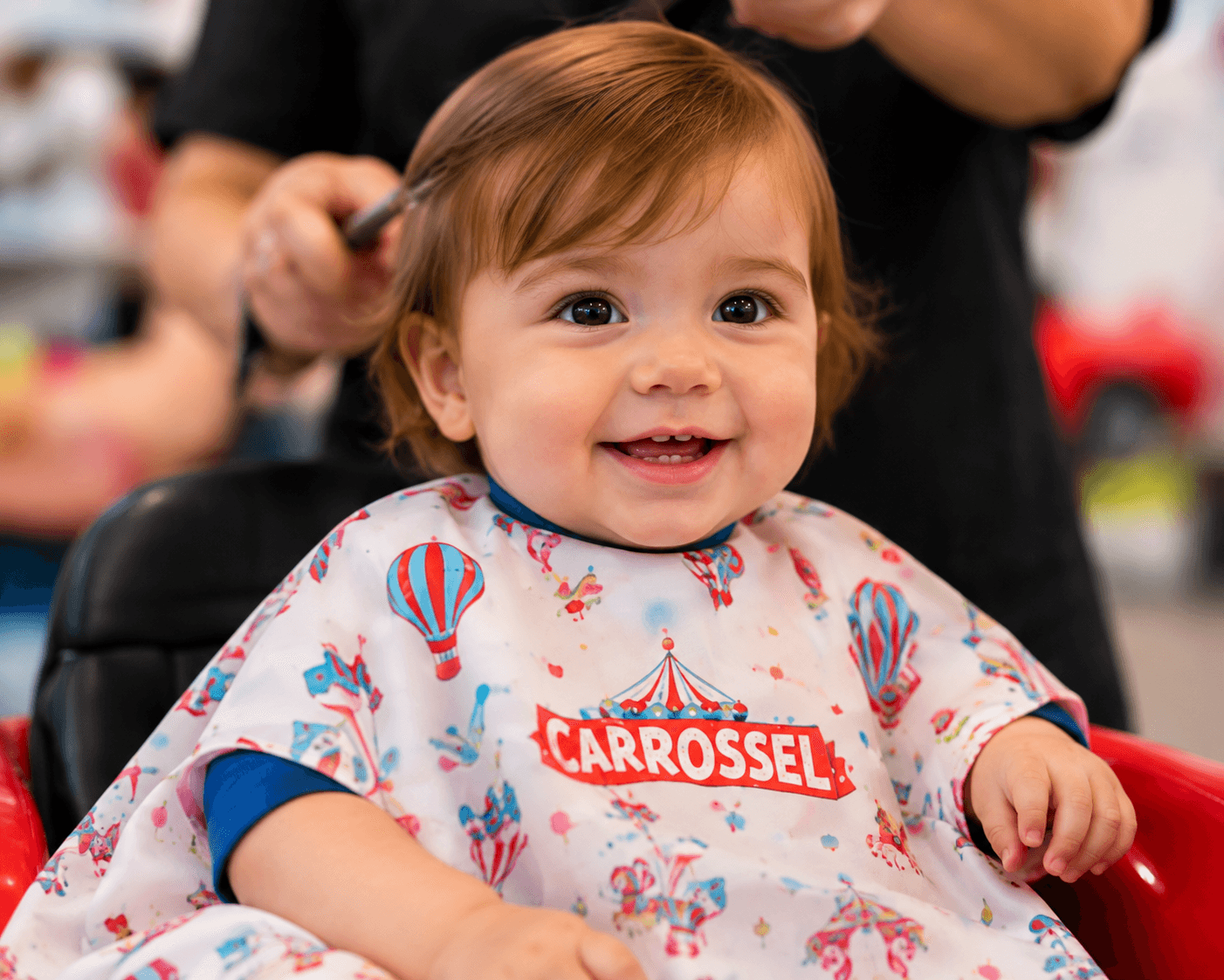Bebé a sorrir com a capa Carrossel, enquanto lhe penteiam o cabelo